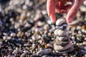 Hand carefully stacking smooth pebbles on a beach, illustrating patience, reflection, and balance in building ethical practice.