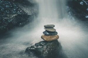 Stacked stones balanced on a rock under flowing water, symbolising equity and resilience in changing systems.